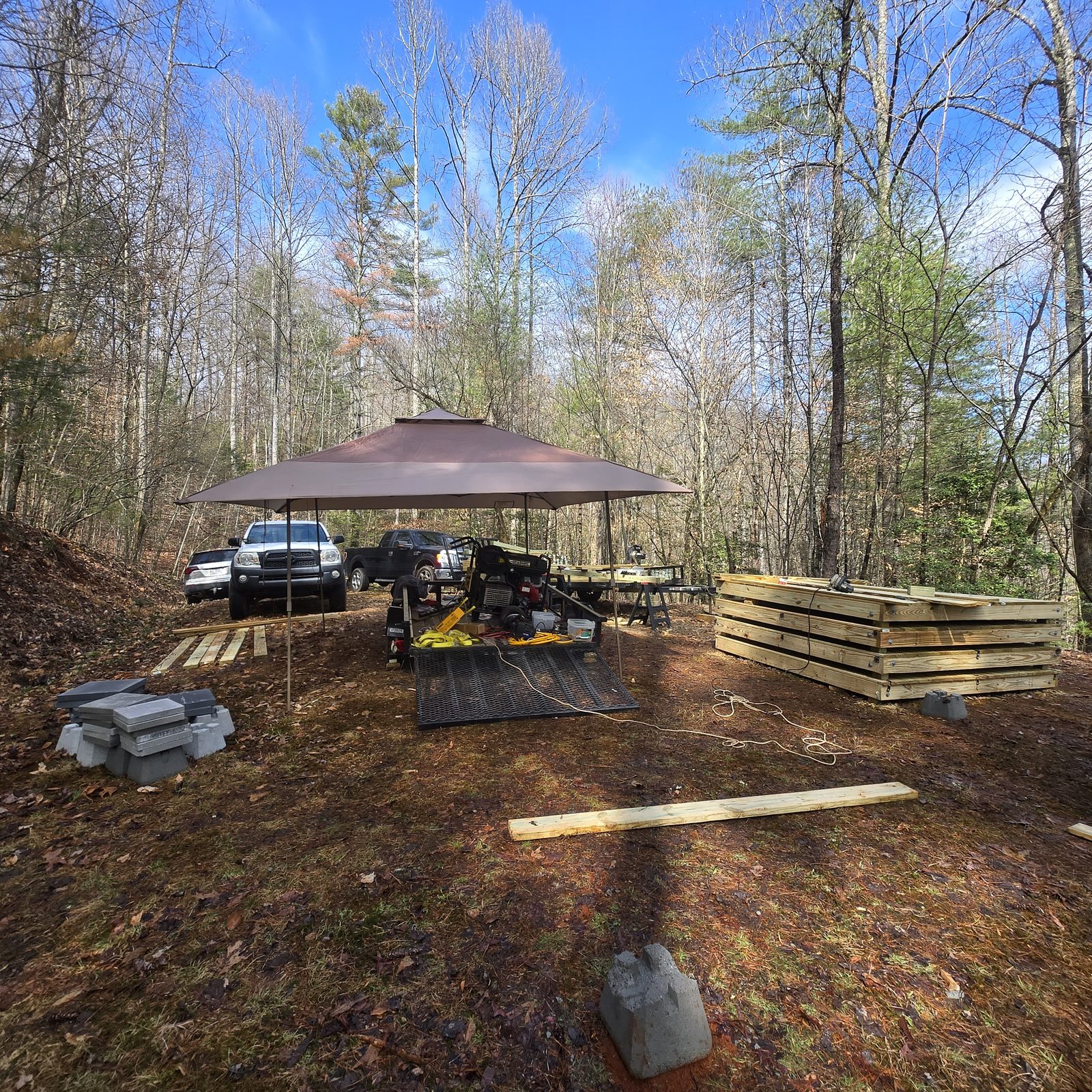 Building tent decks for Cardinal Mountain Campground: a pop-up canopy, trucks and a miter saw in bare winter woods near Franklin, NC