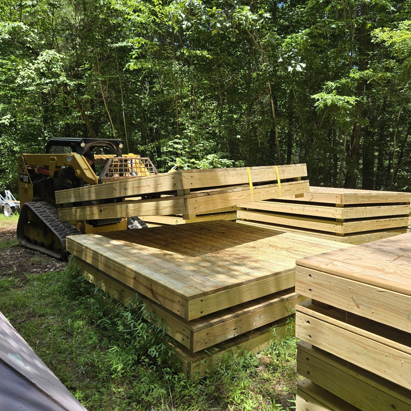 A tracked skid steer beside stacks of finished tent decks at Cardinal Mountain Campground