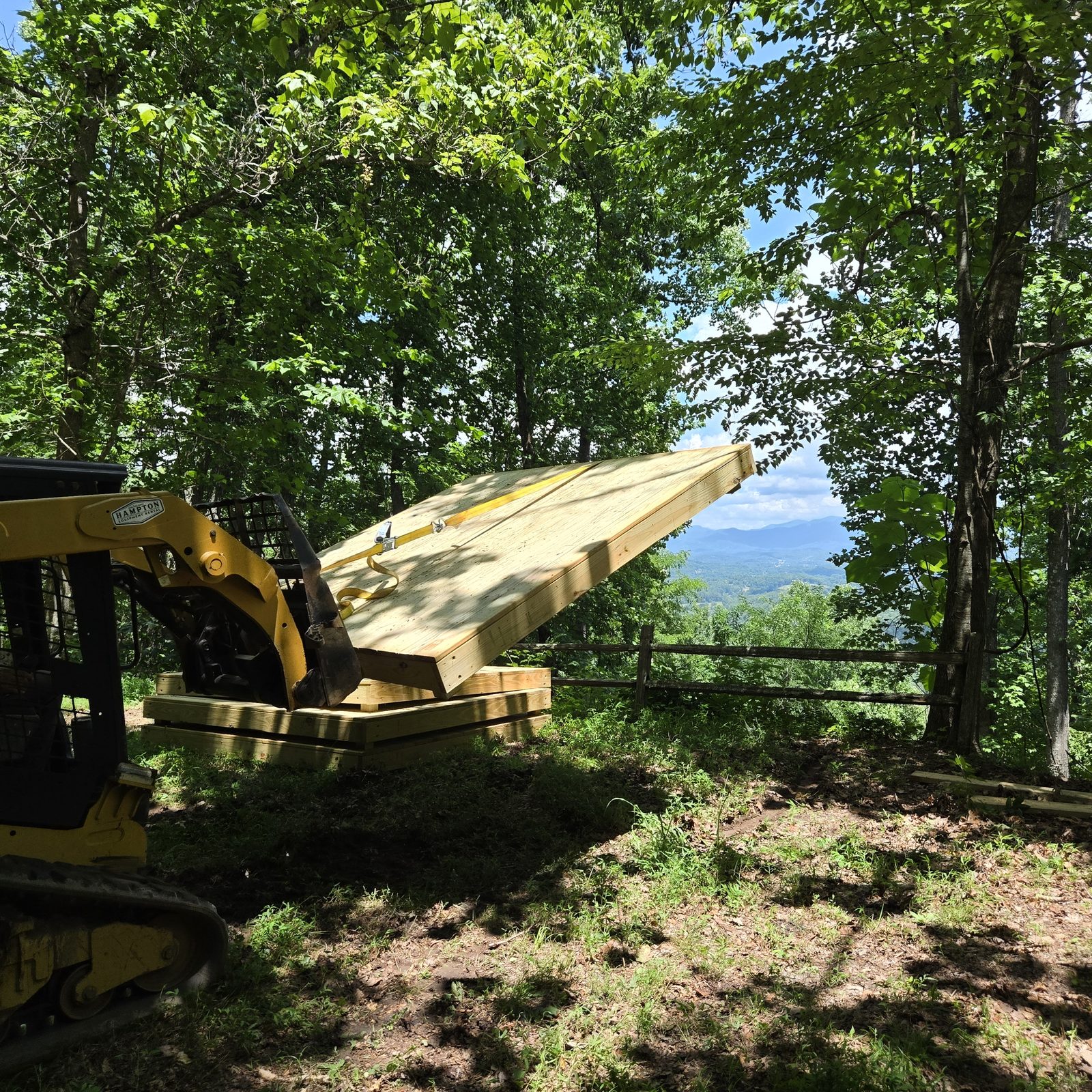 A skid steer placing a wooden tent deck at campsite Smokies 17, Cardinal Mountain Campground, with the Blue Ridge behind