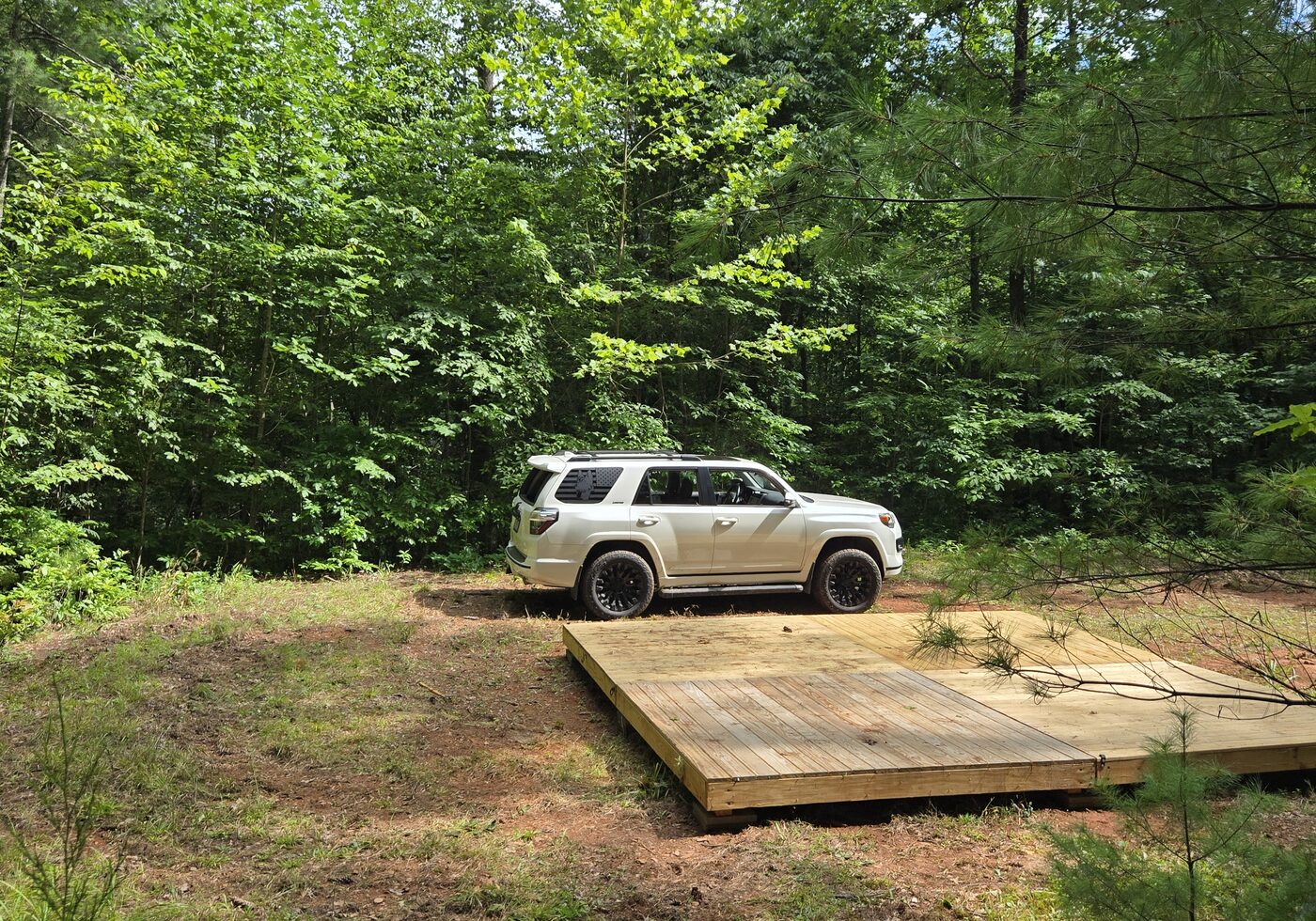 A tent deck at Blue Ridge 1, Cardinal Mountain Campground, with a vehicle parked alongside in the trees