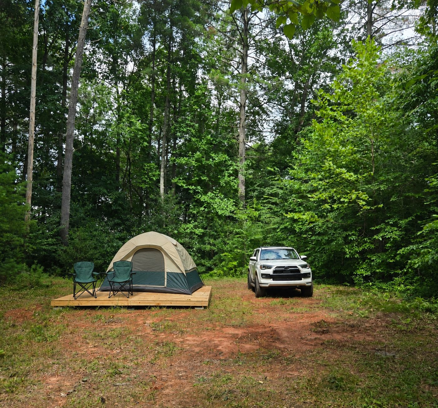 A tent and two camp chairs set up on the wooden deck at Blue Ridge 1, Cardinal Mountain Campground near Franklin NC, with a vehicle parked alongside on the cleared ground