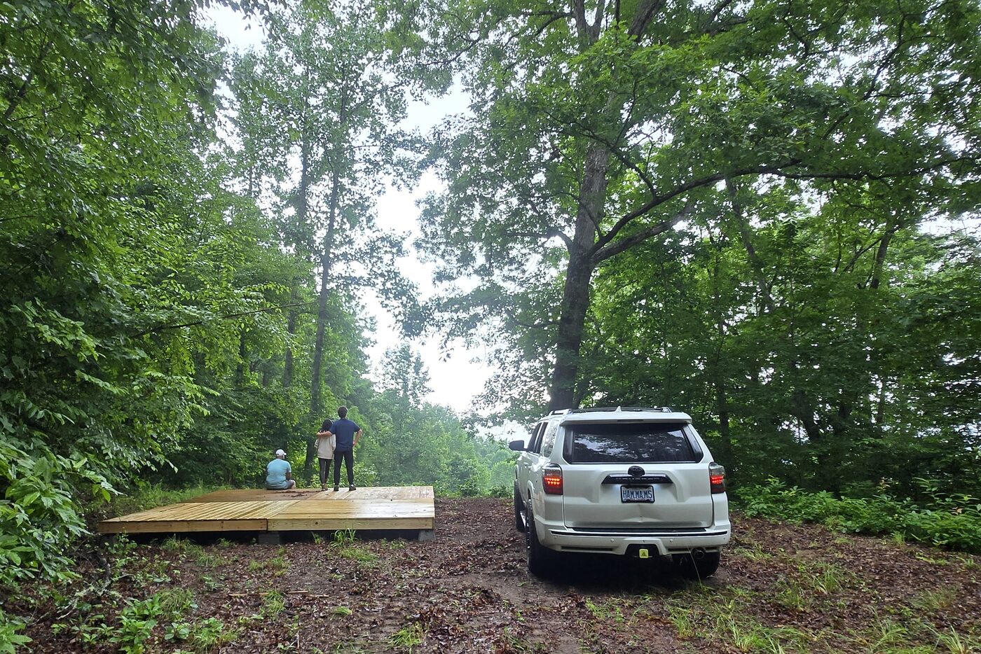 Campers on the deck at Katahdin 9, Cardinal Mountain Campground, with a vehicle parked alongside