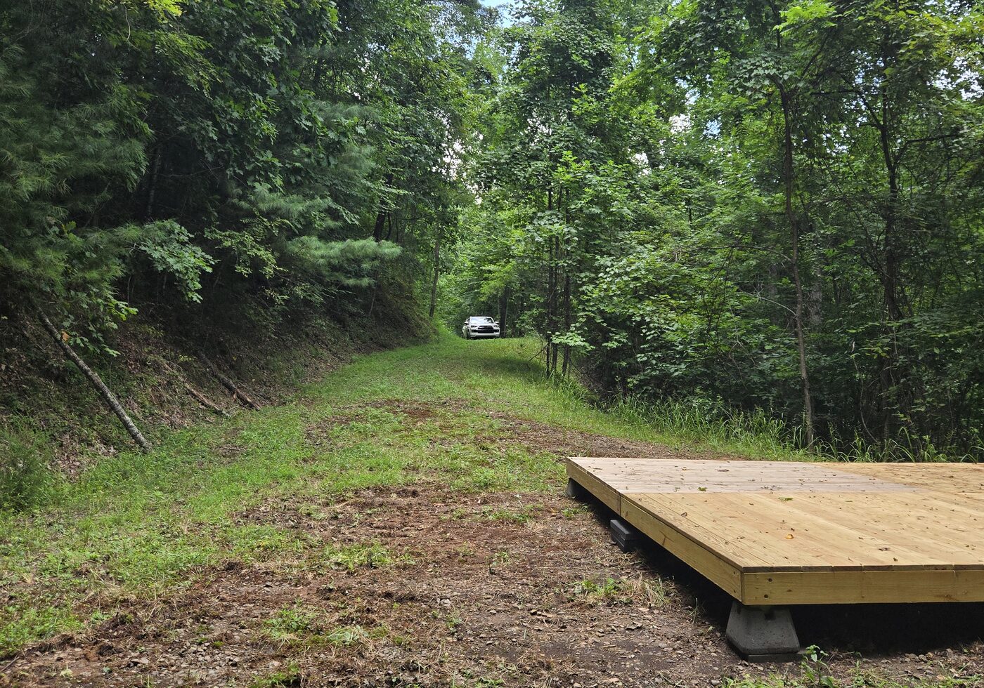 The deck and pull-in at Redwood 12, Cardinal Mountain Campground, with a vehicle parked up the drive