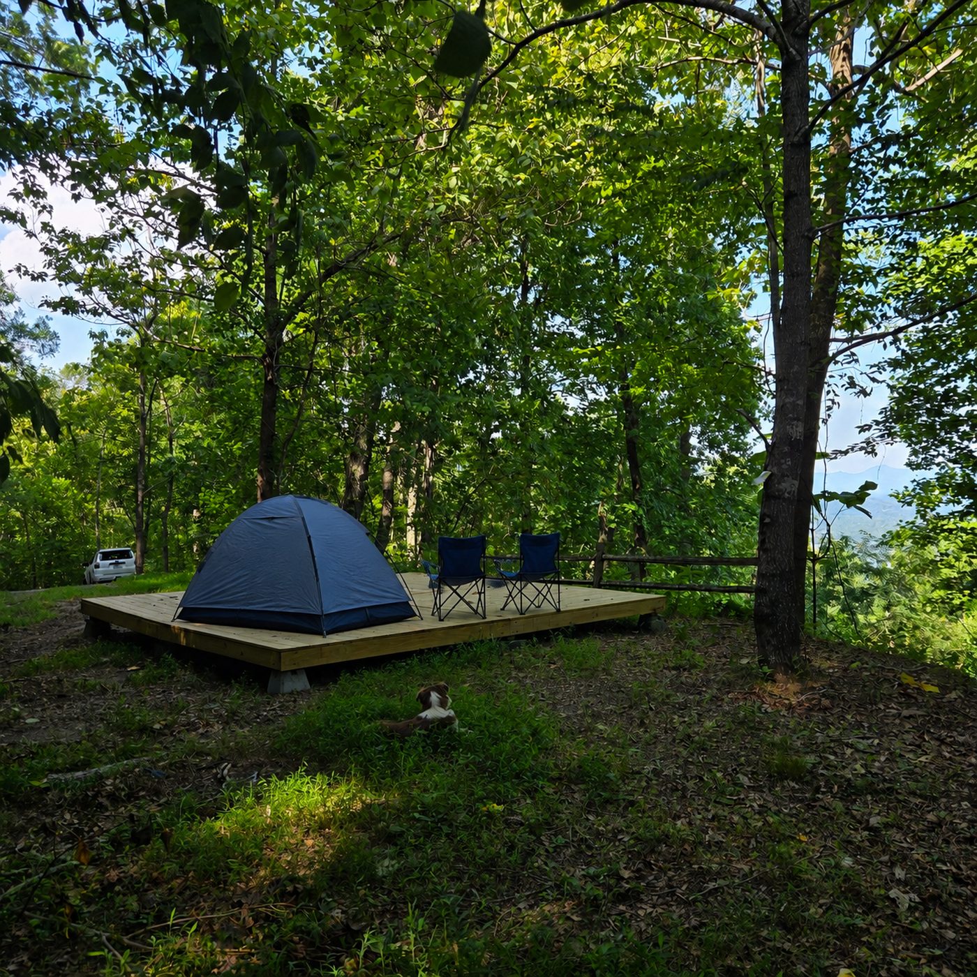 A tent and two camp chairs on the deck at Smokies 17, Cardinal Mountain Campground near Franklin NC, with a split-rail fence running along the edge of the site